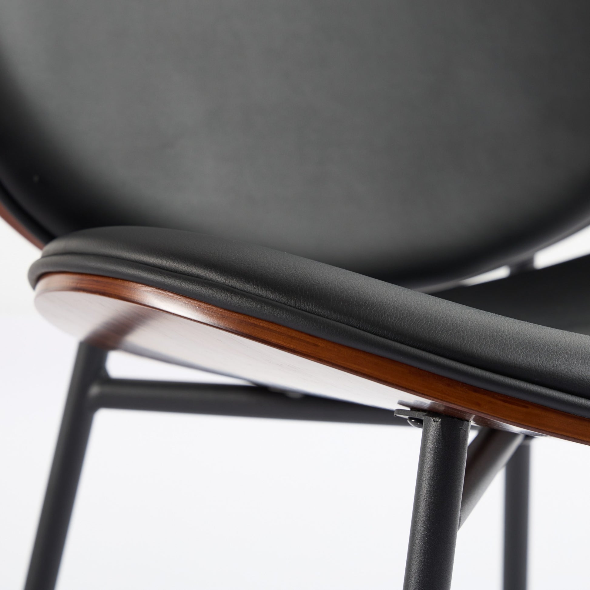 Closeup of black faux leather chair seat with wood trim and metal legs