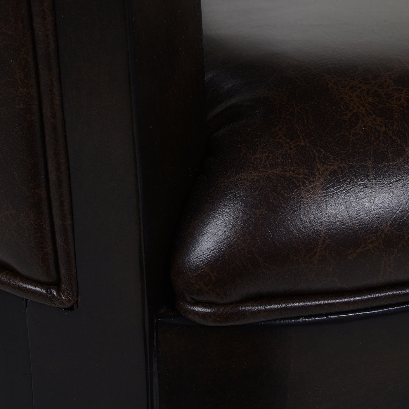Dark brown leather armchair detail with tufted seat and wooden frame