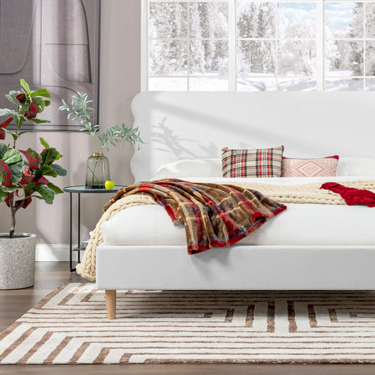 Cozy white upholstered bed with a textured headboard and plaid throw blanket