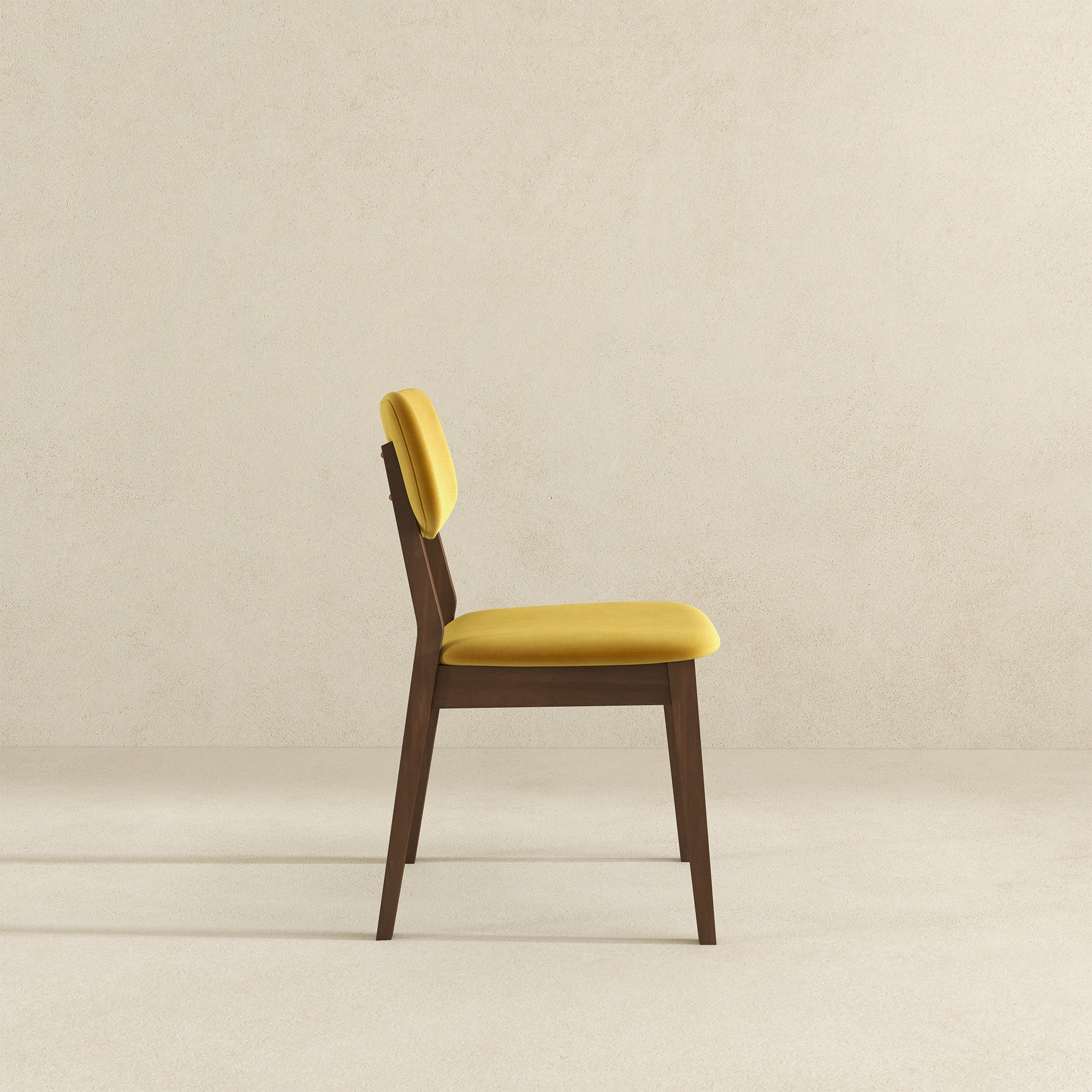 Side profile of a modern yellow velvet upholstered dining chair with dark wood frame