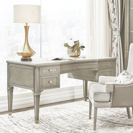 Gray wood writing desk with ornate hardware and drawers complementing a plush armchair and lamp