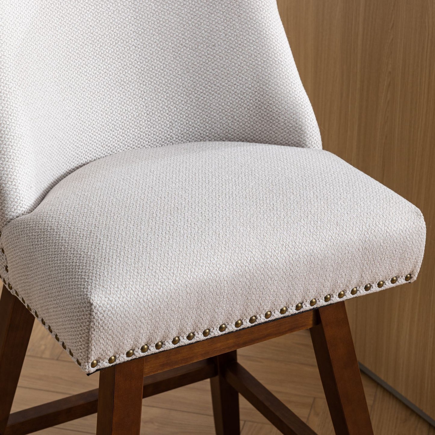 Closeup of a light beige upholstered dining chair with brass nailhead trim and dark wood legs