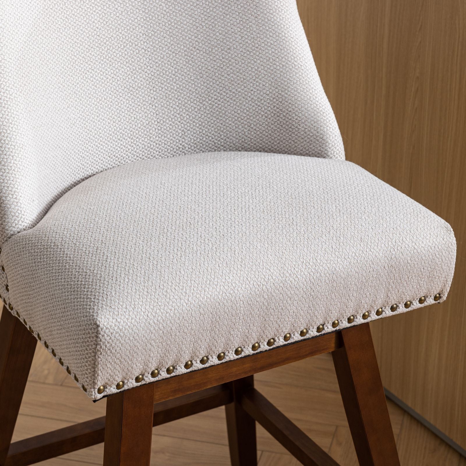 Closeup of a light beige upholstered dining chair with brass nailhead trim and dark wood legs