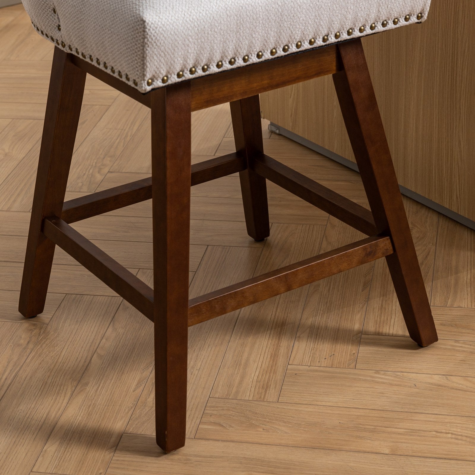 Upholstered bar stool with a neutral textured seat and dark wood legs featuring decorative nailhead trim