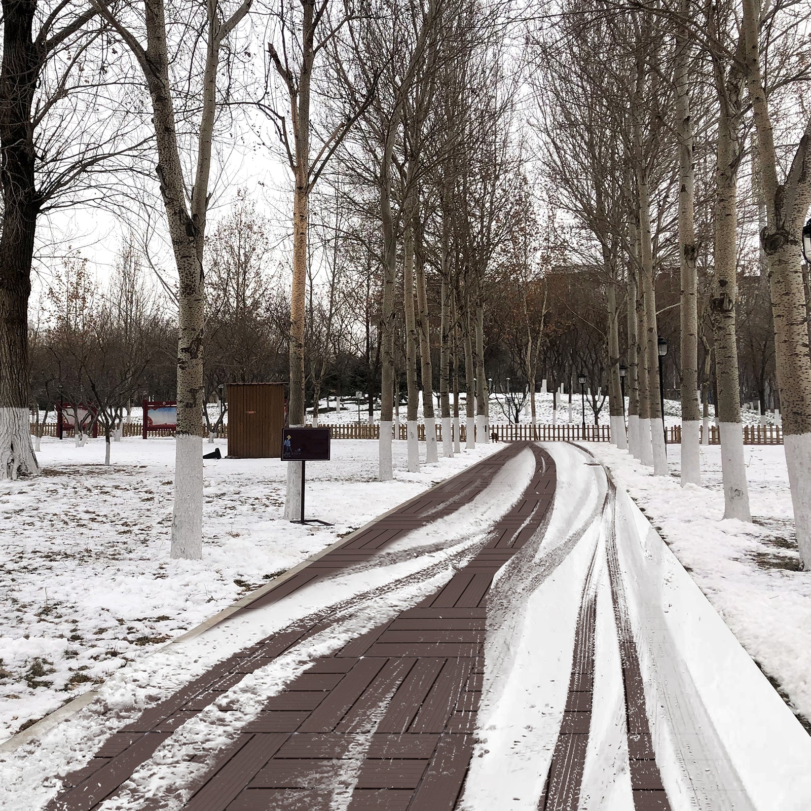 Wooden park walkway with snow tire tracks and bare trees