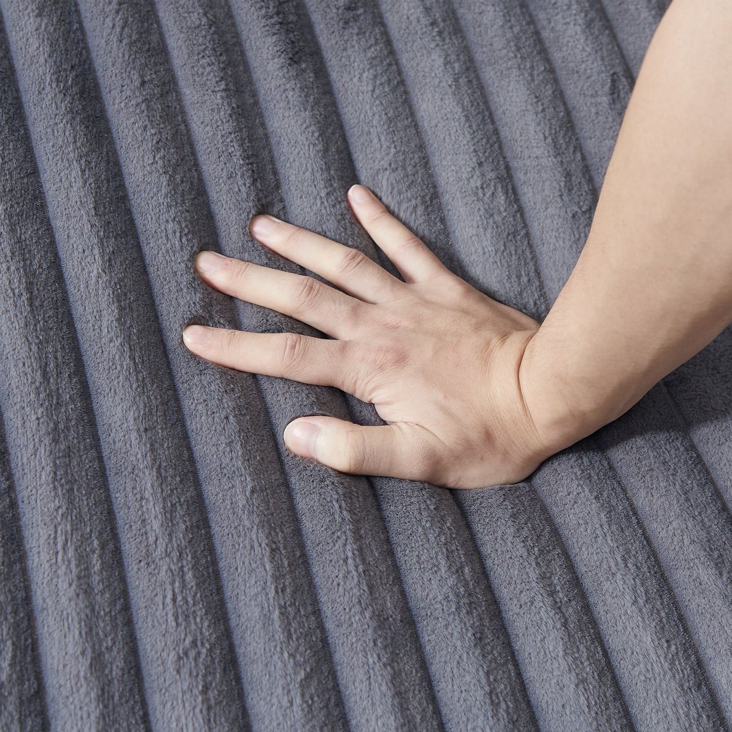 Hand pressing into plush grey ribbed velvet fabric showcasing softness
