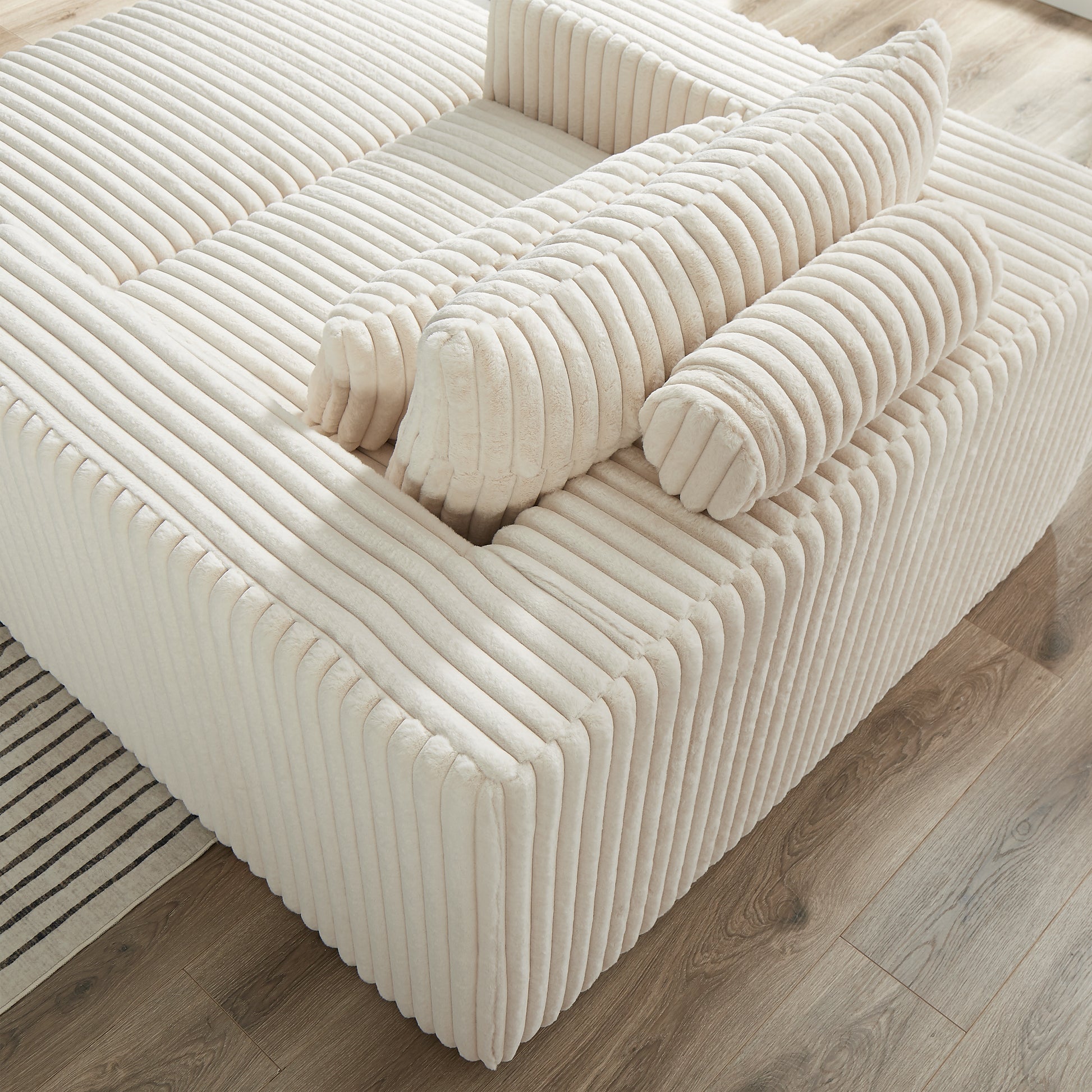 Plush ivory corduroy sectional sofa with rolled accent pillows on a wood floor