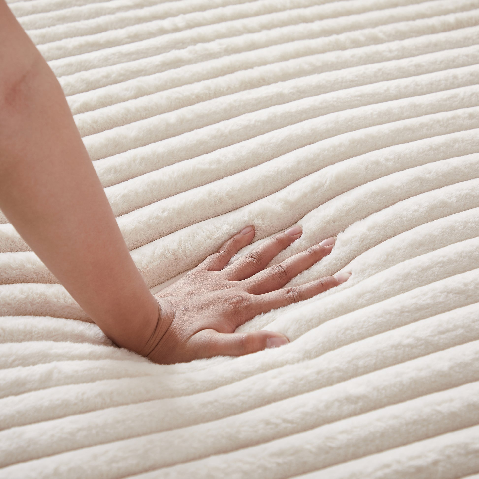 Creamy white plush throw blanket with deep ribbed texture hand pressing down