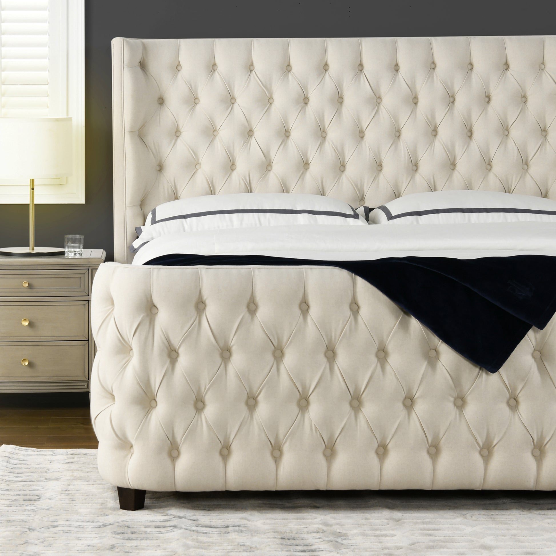 Cream tufted upholstered bed with diamond button detailing and navy velvet throw