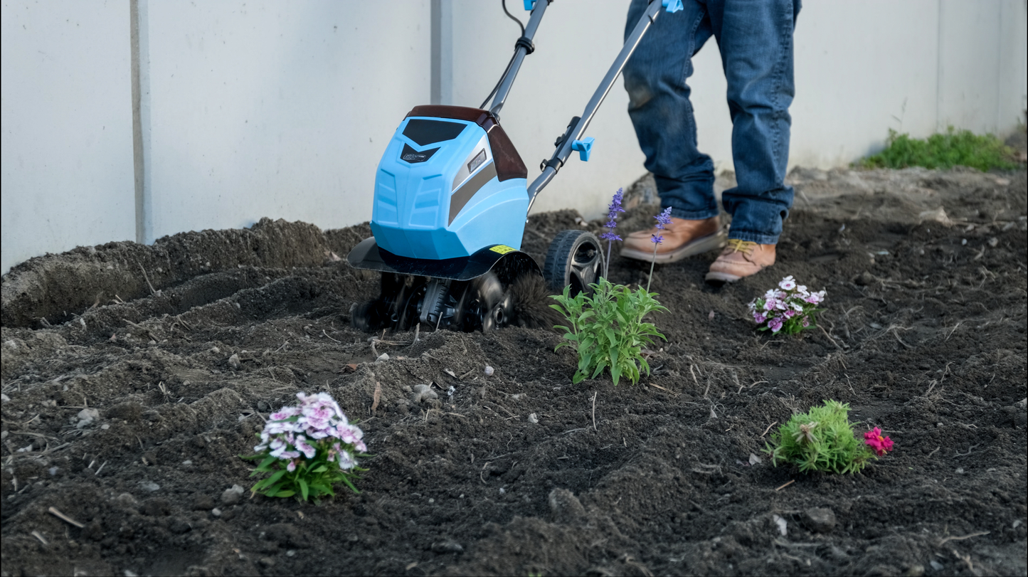 Blue electric tiller with rotating tines breaking up soil for gardening preparation