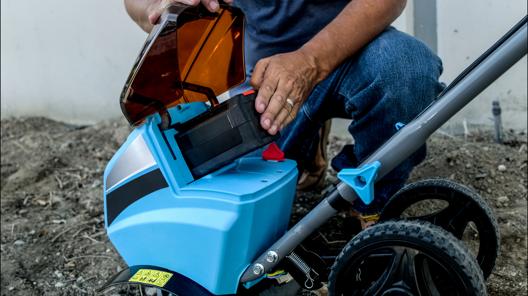 Person inserting battery into a blue electric tiller for yard work