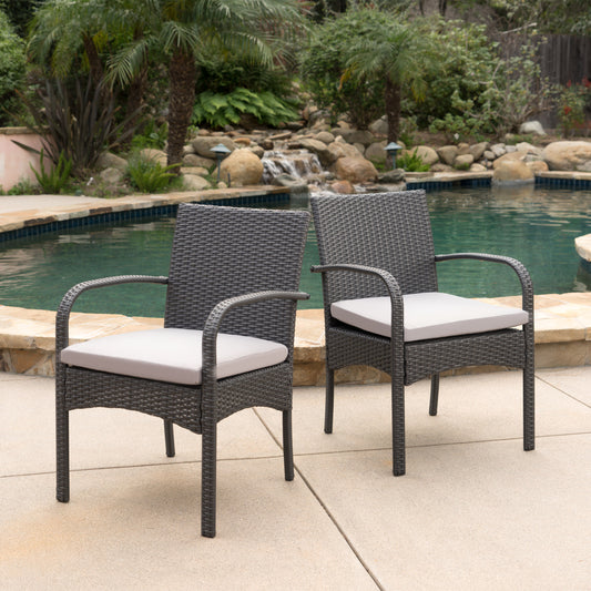 Two dark grey wicker dining chairs with light grey cushions placed by a pool