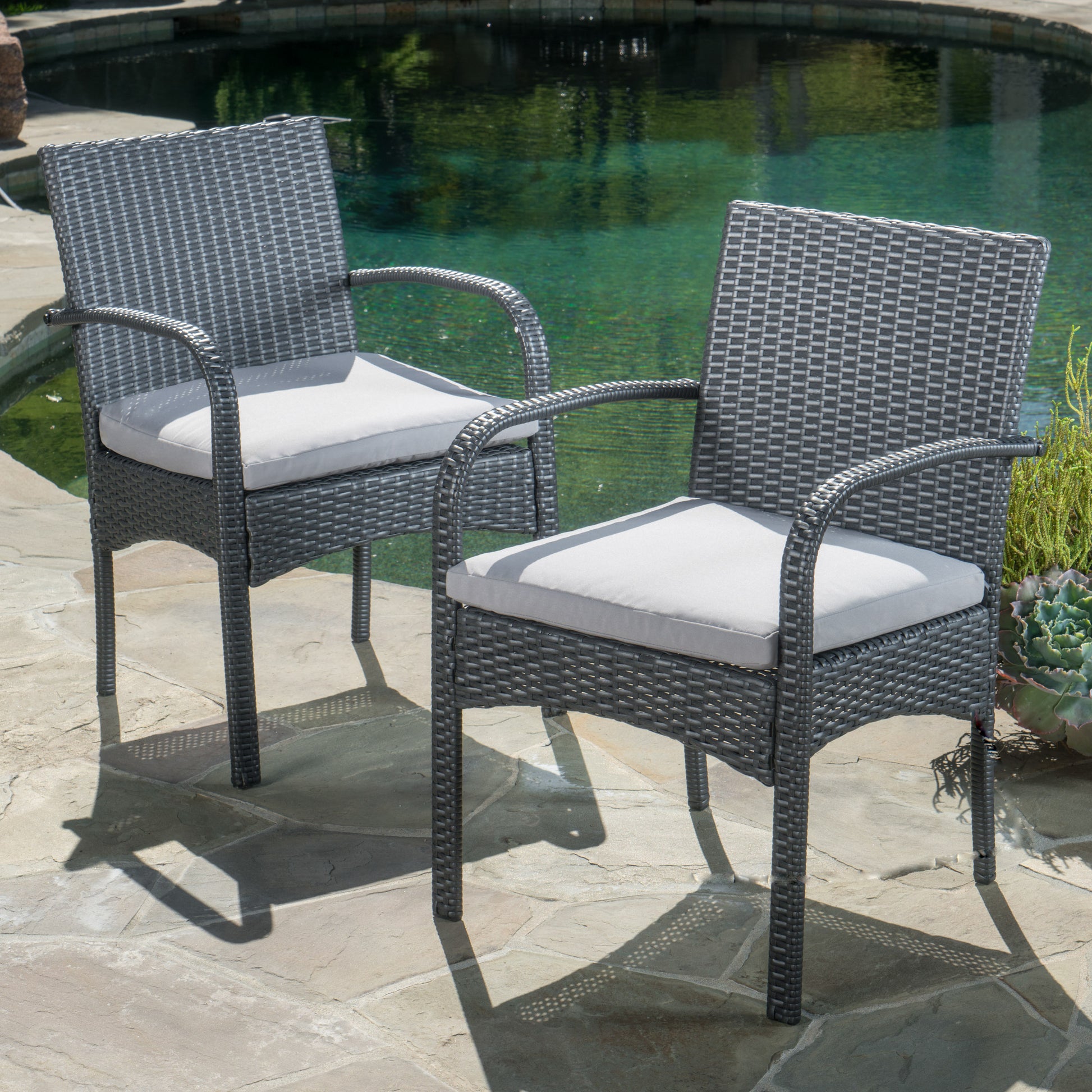 Two gray wicker outdoor dining chairs with light gray cushions beside a pool