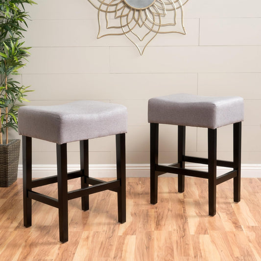 Two grey upholstered backless bar stools with dark wood legs and a saddle seat design