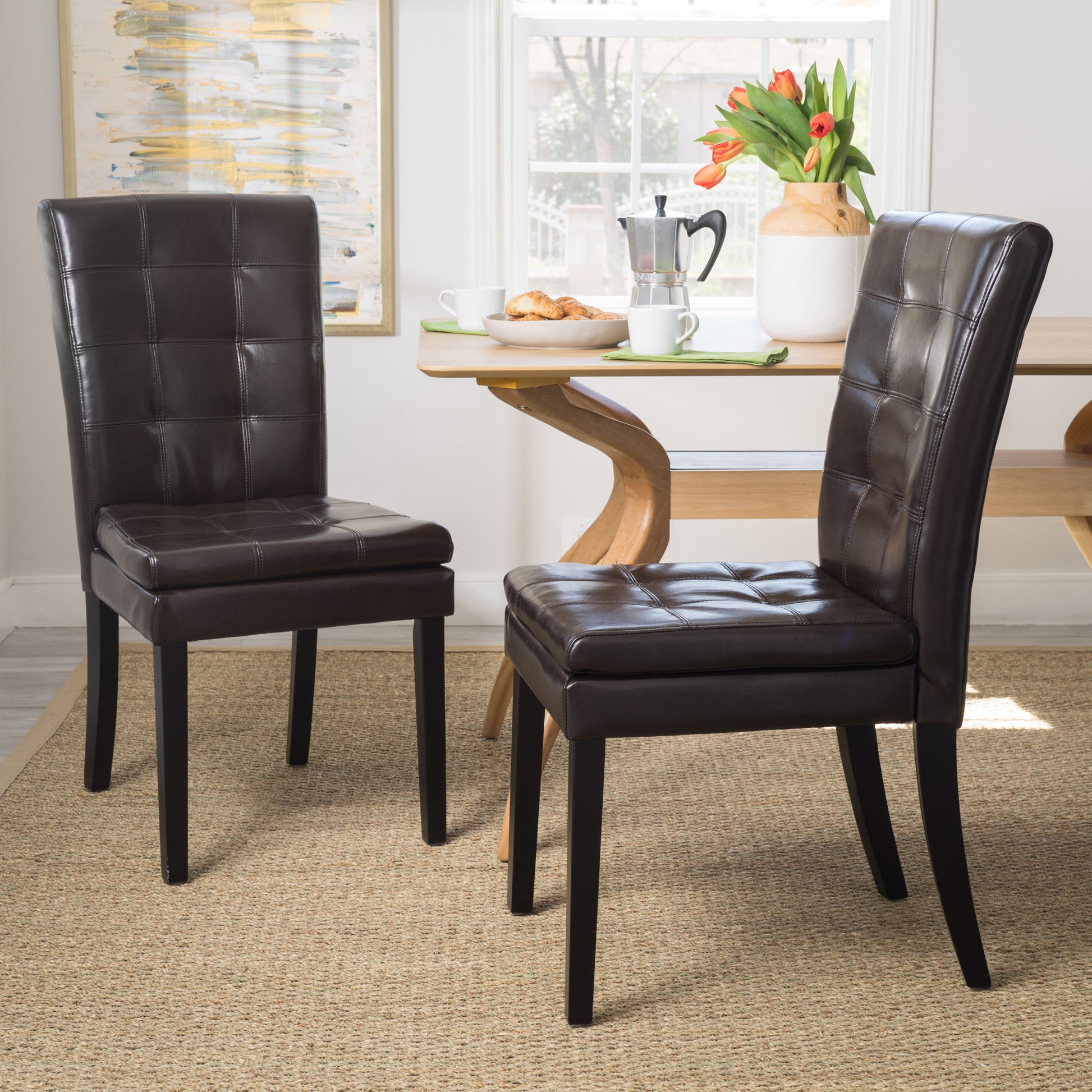 Two dark brown faux leather dining chairs with tufted backs and seats