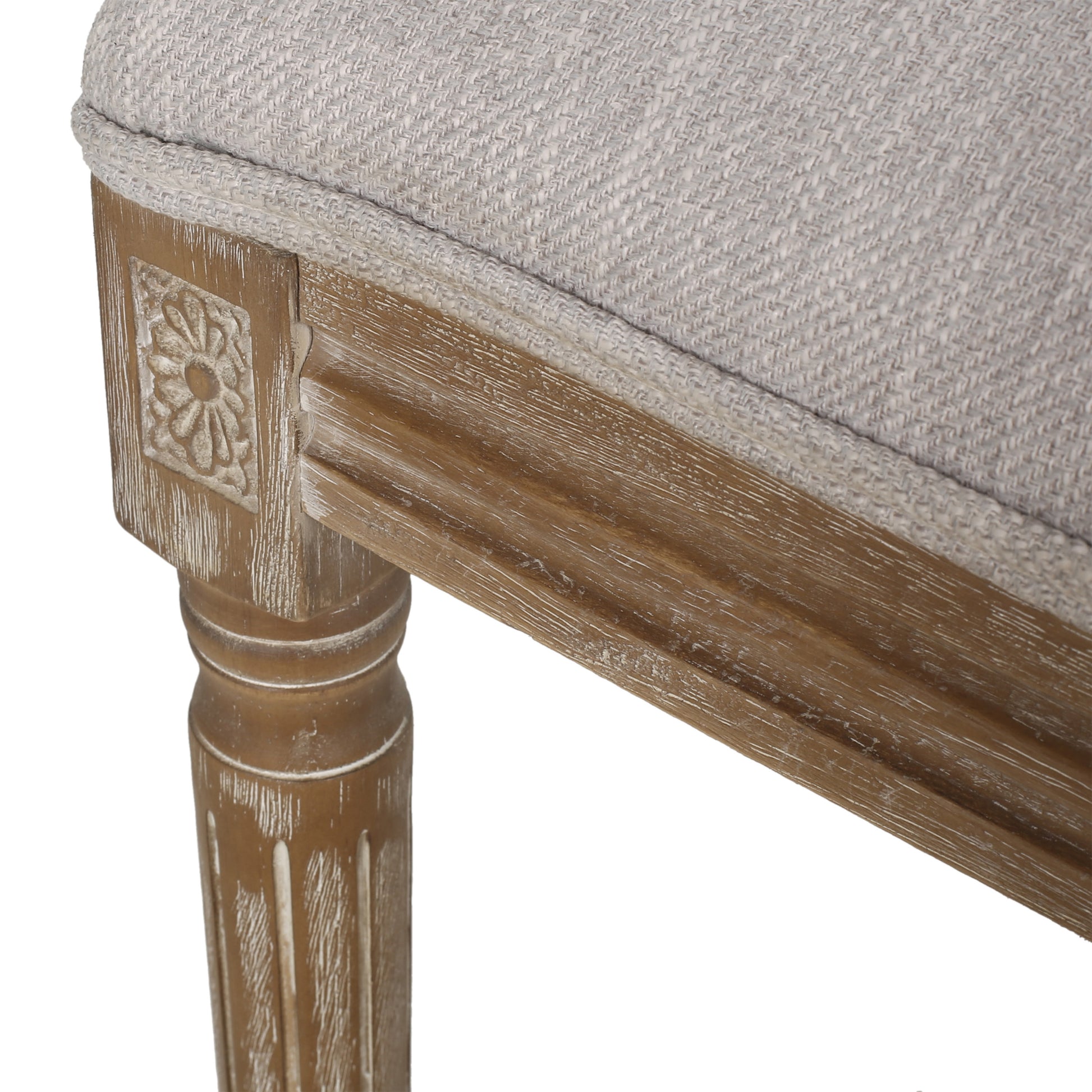 Closeup of a textured light gray woven fabric cushion on a rustic distressed wood bench leg with carved detail