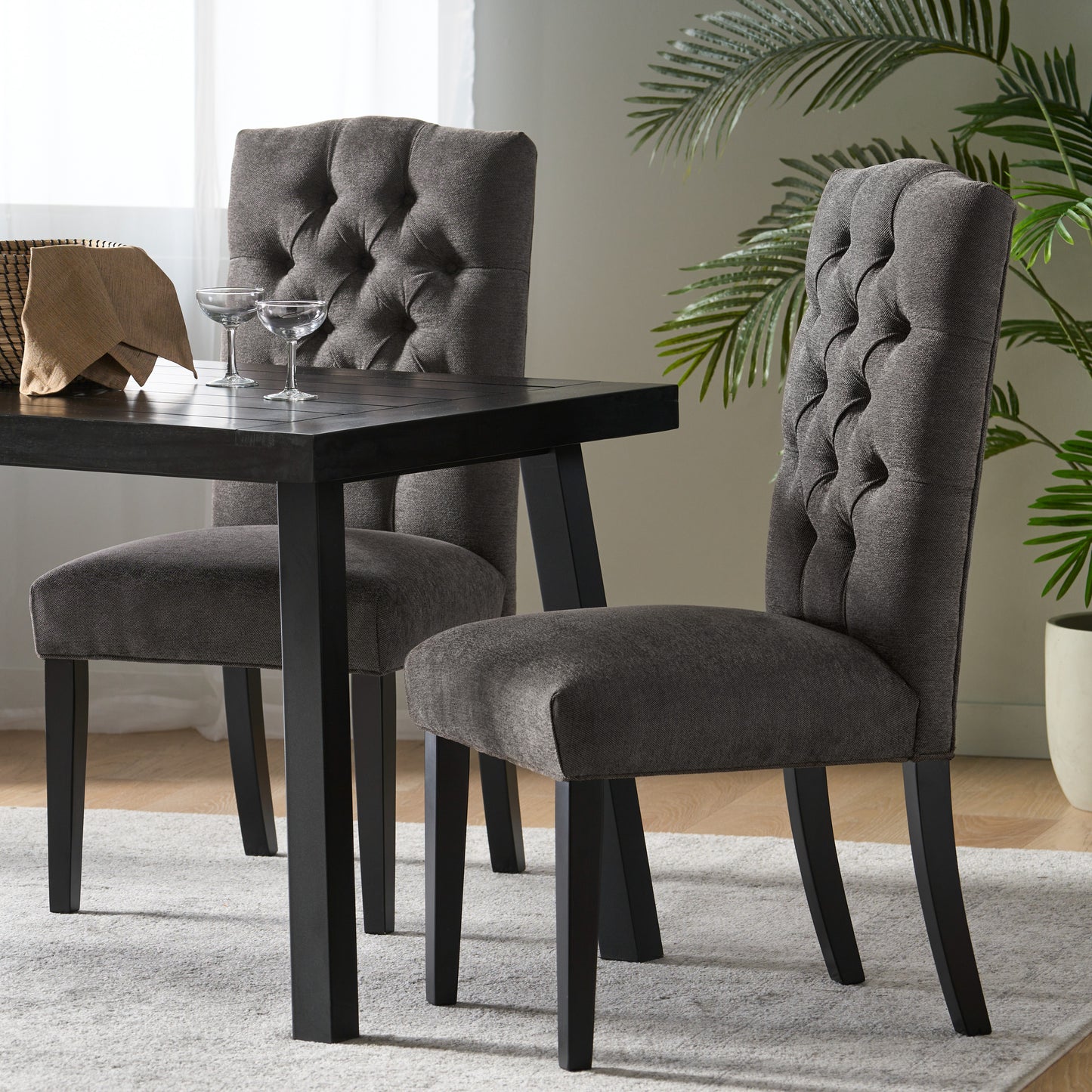 Two dark grey upholstered dining chairs with tufted backs sit at a dark wood table