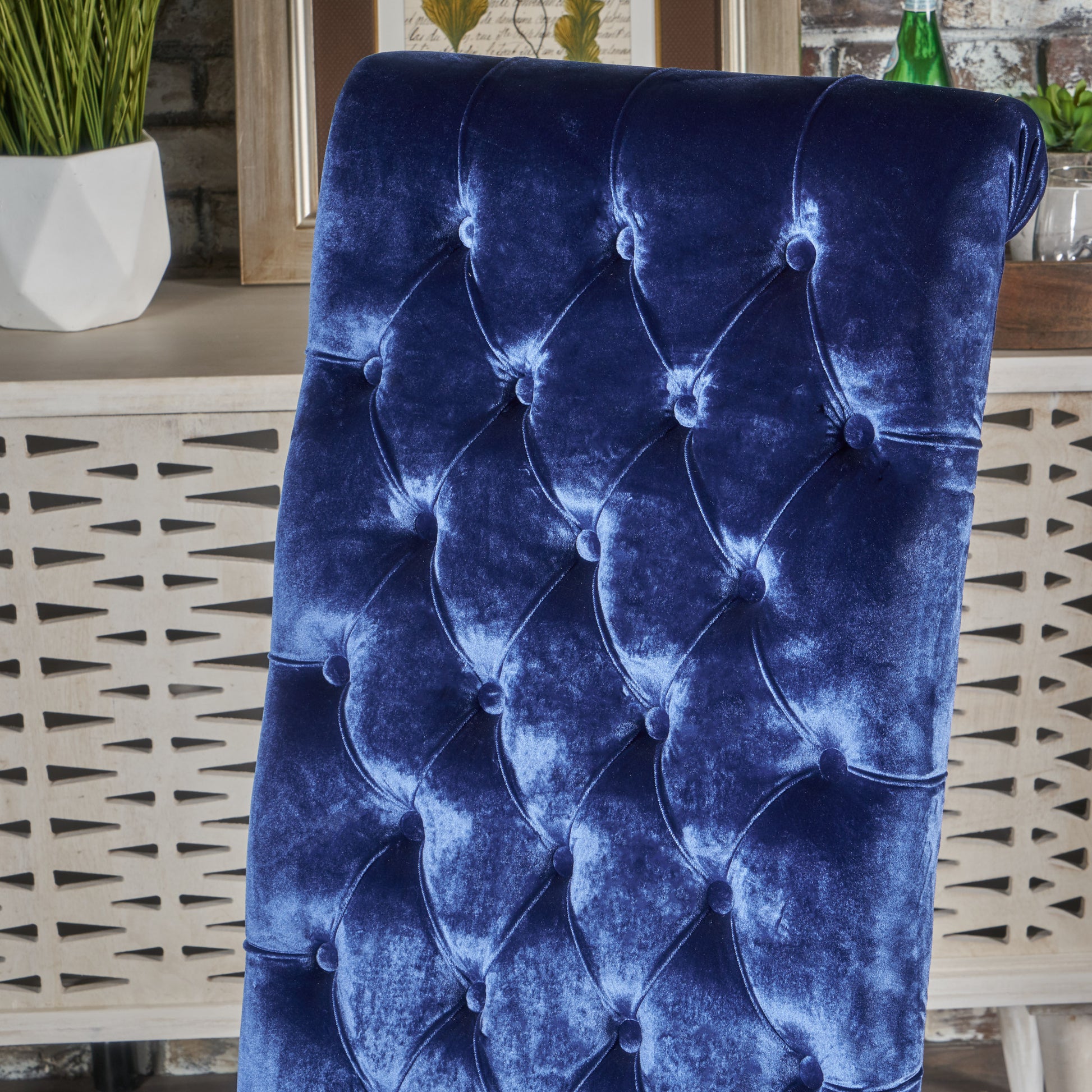 Closeup of deep blue velvet tufted chair back with diamond stitching and antique brass nails