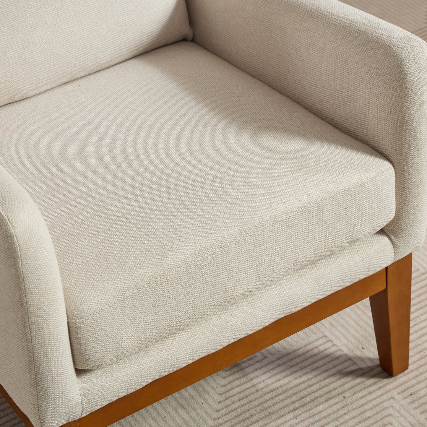 Closeup of a creamcolored armchair seat with a textured fabric and wooden legs