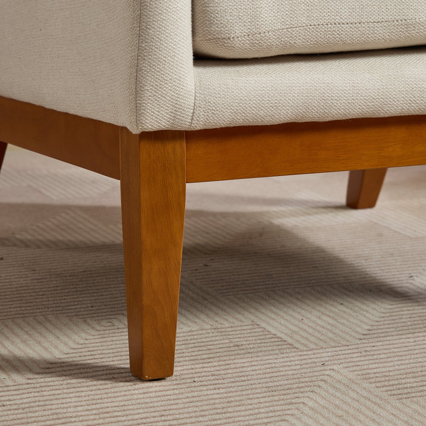Closeup of a beige textured sofa arm with sturdy wooden legs