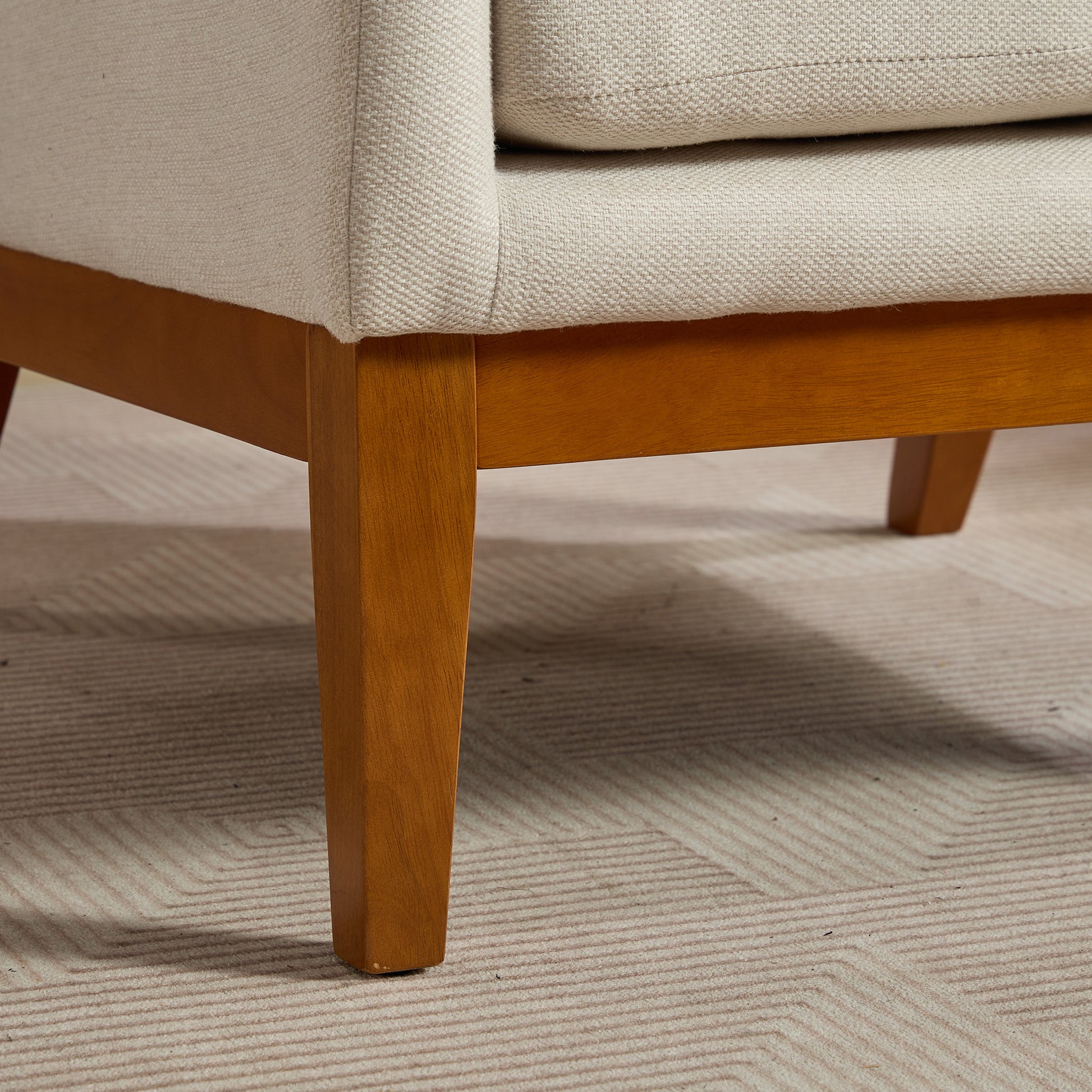 Closeup of a beige textured sofa arm with sturdy wooden legs