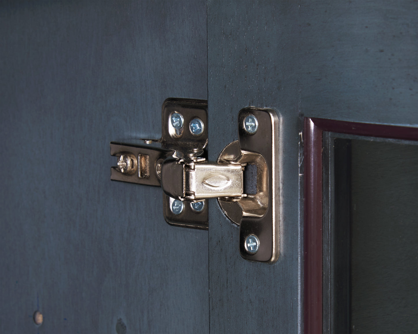 Closeup of brass cabinet hinge on a dark blue painted wooden door