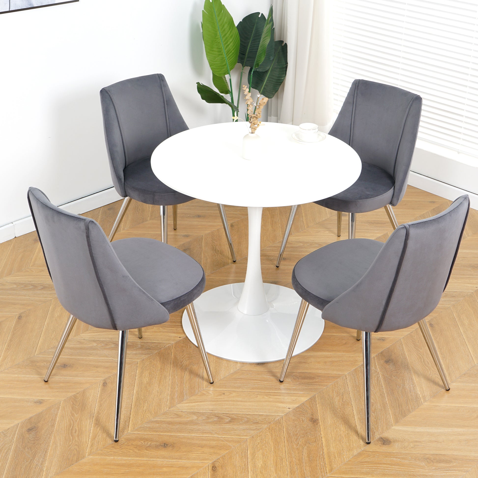 Modern grey velvet dining chairs with chrome legs around a white tulip table