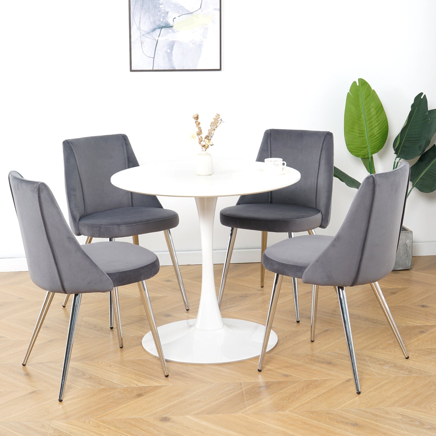 Four plush gray velvet dining chairs with chrome legs surround a white tulip dining table
