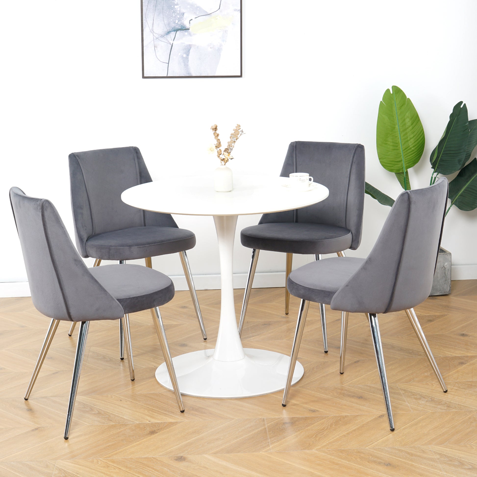 Four plush gray velvet dining chairs with chrome legs surround a white tulip dining table