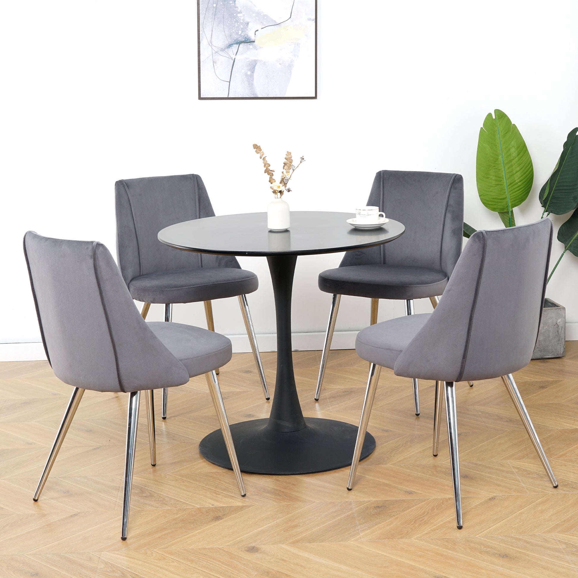 Four grey velvet dining chairs with chrome legs surrounding a black tulip table