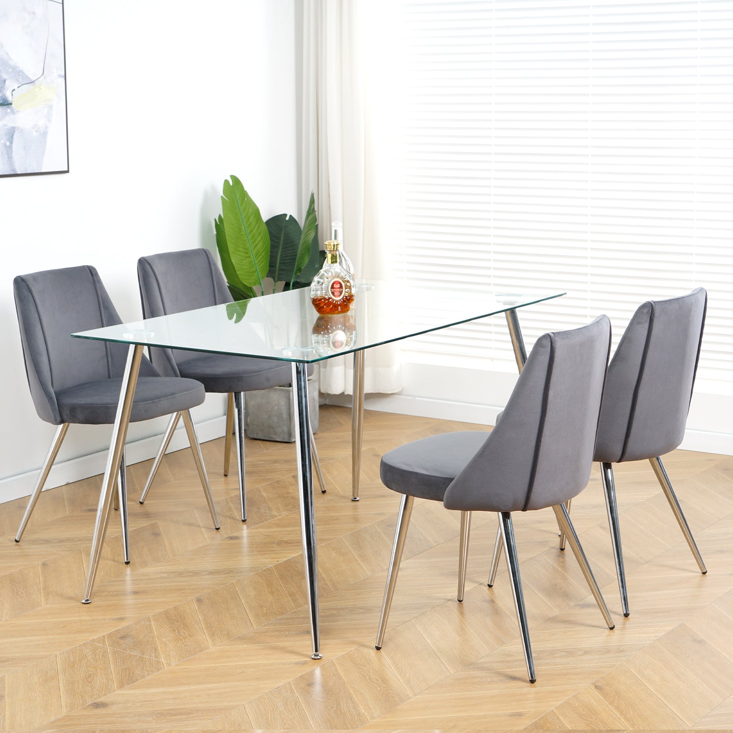 Modern dining set with clear glass tabletop and four grey velvet chairs with chrome legs