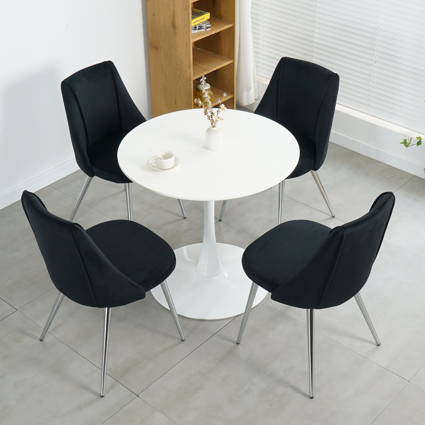 Four black velvet dining chairs with chrome legs arranged around a white tulip table