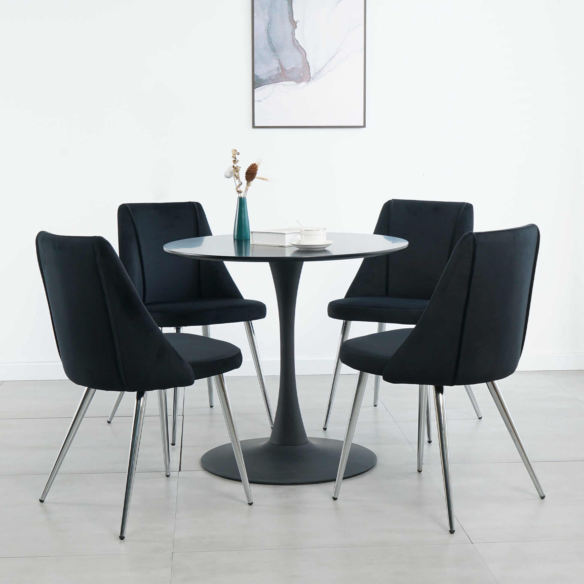 Four black velvet dining chairs with chrome legs around a round pedestal table