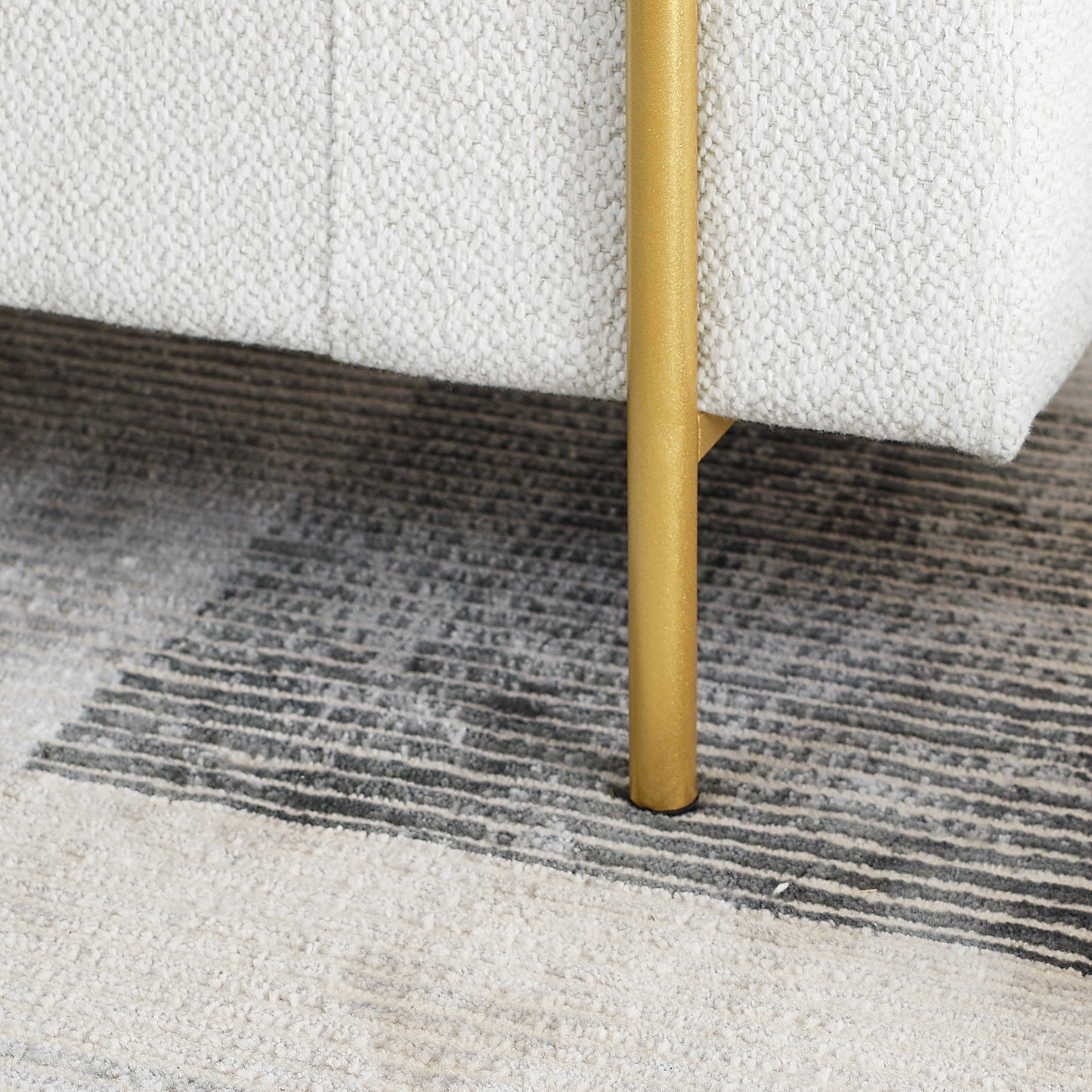 Closeup of cream textured fabric sofa corner with a gold metal leg on a striped rug