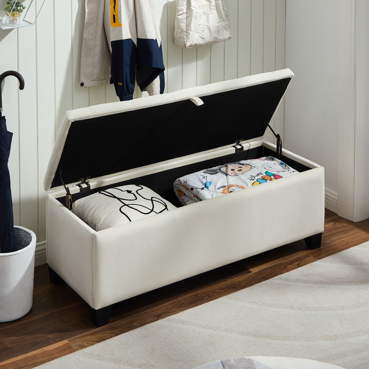 Cream velvet storage ottoman with open lid revealing pillows and blanket