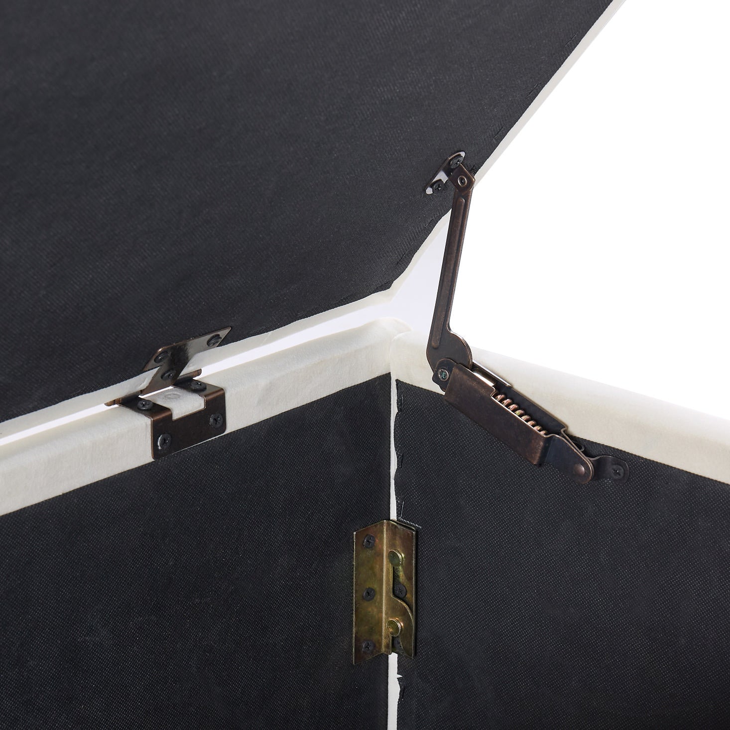 Closeup of dark fabric lining with antique brass lid support hinges on an ottoman