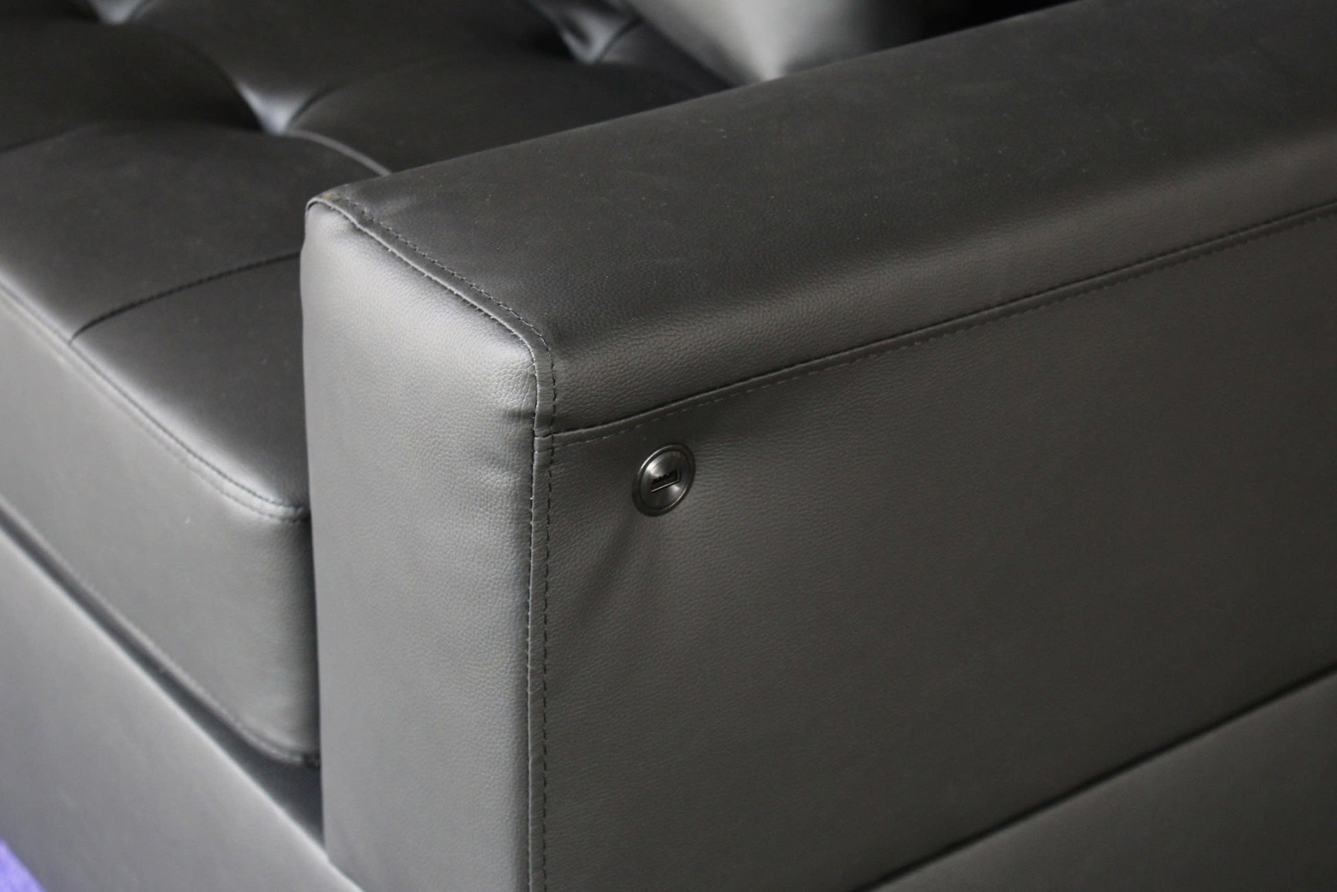 Black faux leather sofa armrest with detailed stitching and a circular metal accent