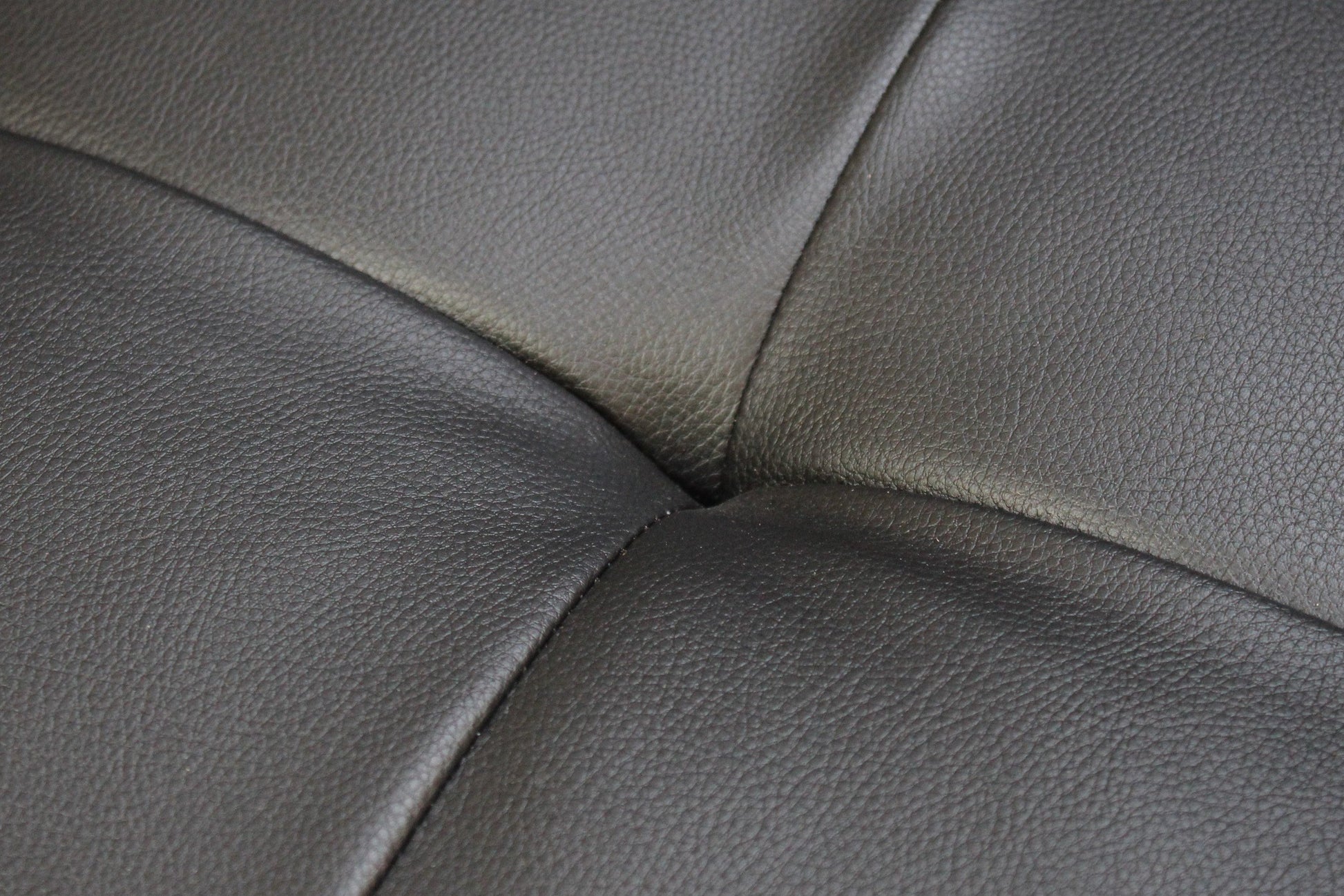 Closeup of dark grey textured leather sofa upholstery with visible stitching