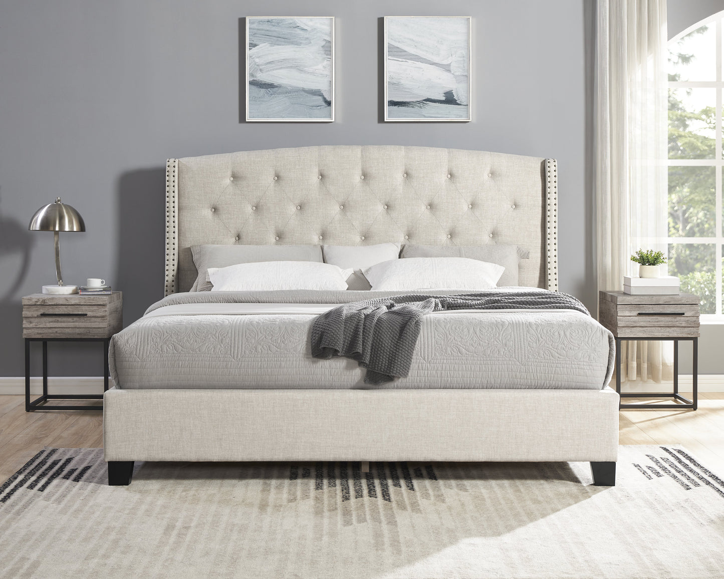 Beige upholstered tufted bed with nailhead trim headboard and neutral bedding