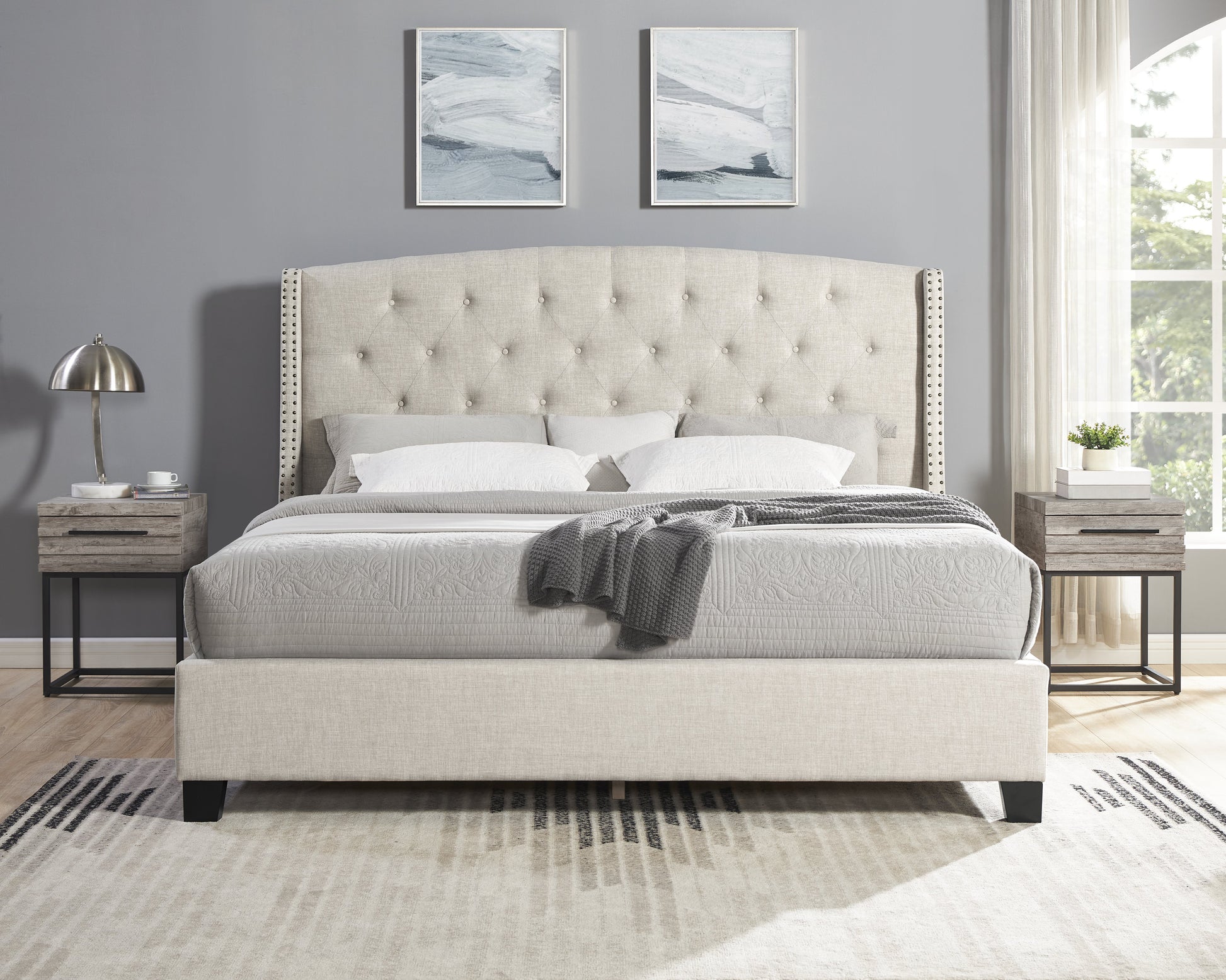 Beige upholstered tufted bed with nailhead trim headboard and neutral bedding
