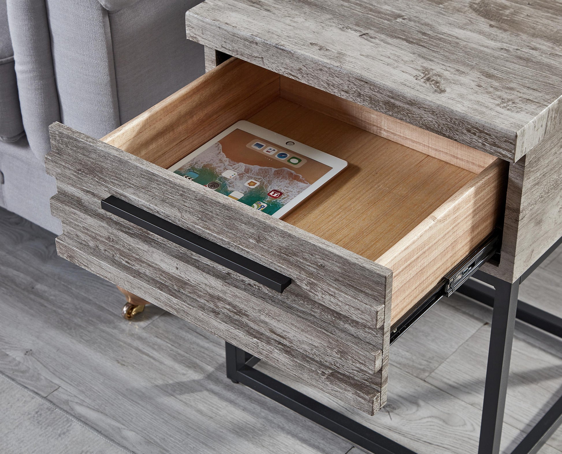 Distressed grey wood end table with open drawer revealing a tablet