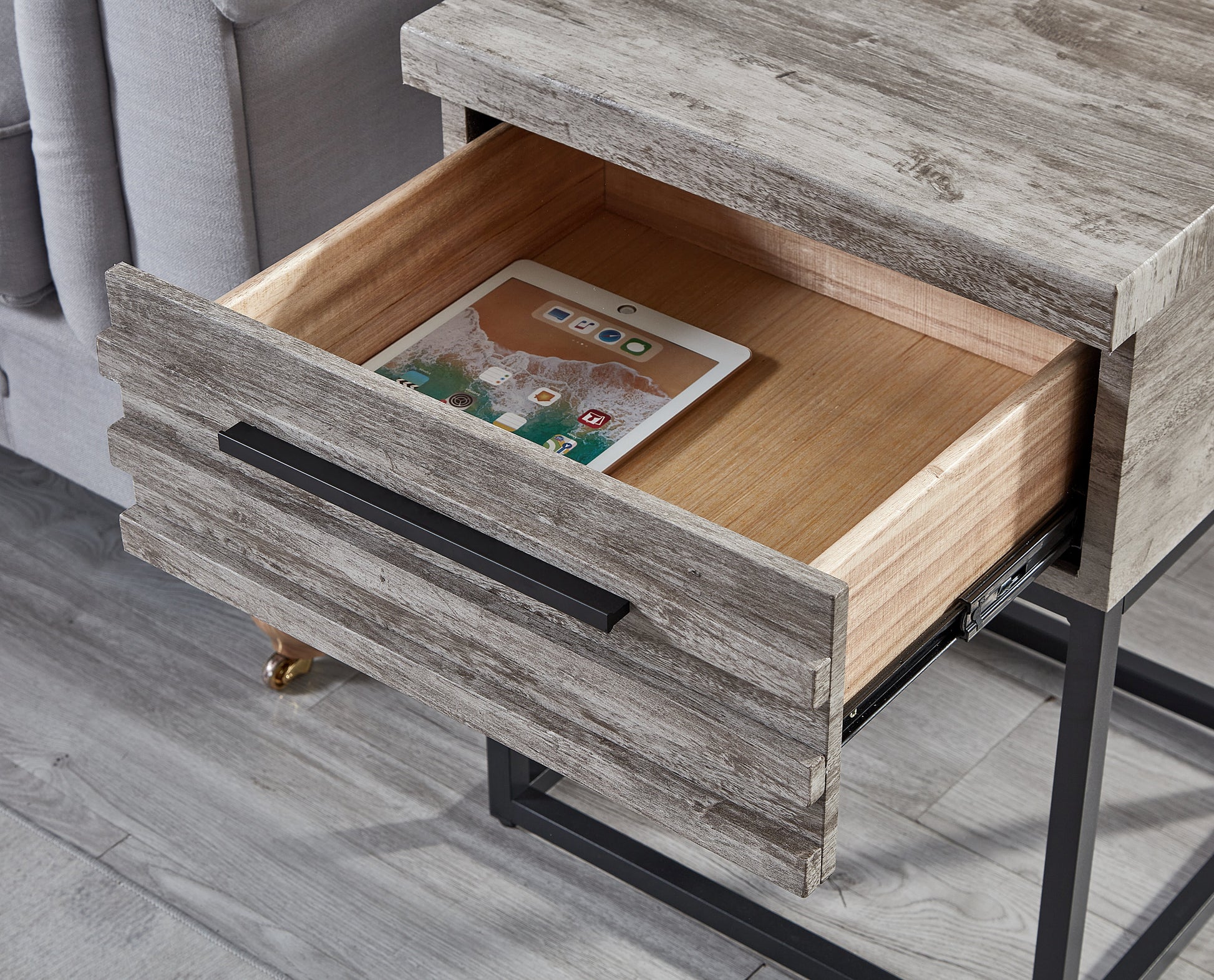 Rustic gray wash wood end table with open drawer holding a tablet