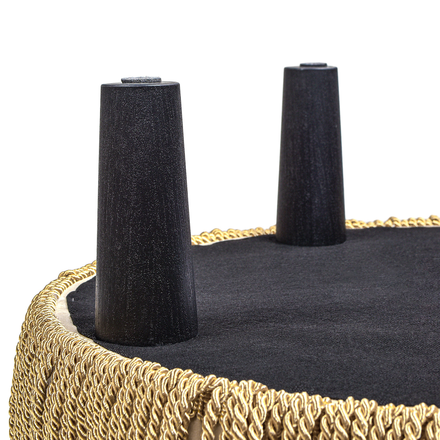 Two tapered black wooden legs on a black upholstered ottoman with gold fringe trim