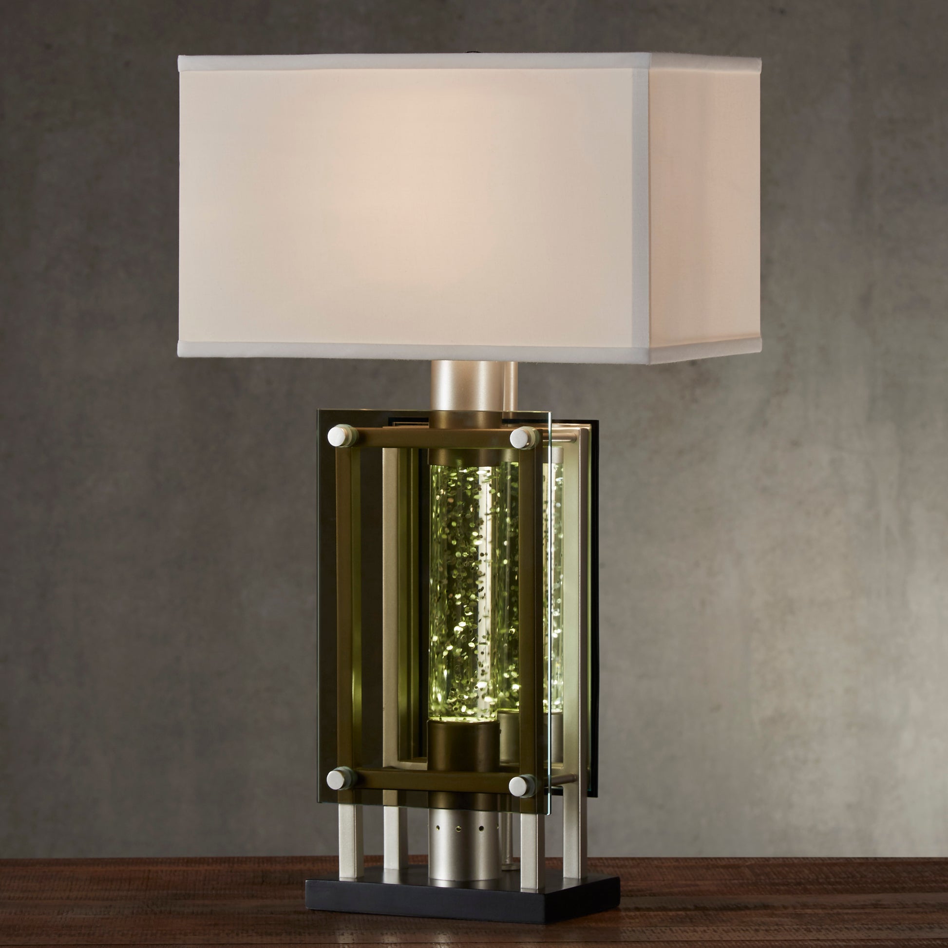 Modern desk lamp with a clear glass cylinder filled with shimmering golden accents
