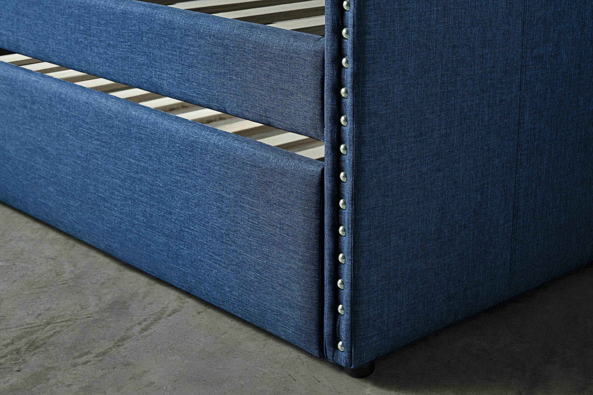 Closeup of a navy blue upholstered bed frame with silver nailhead trim detailing