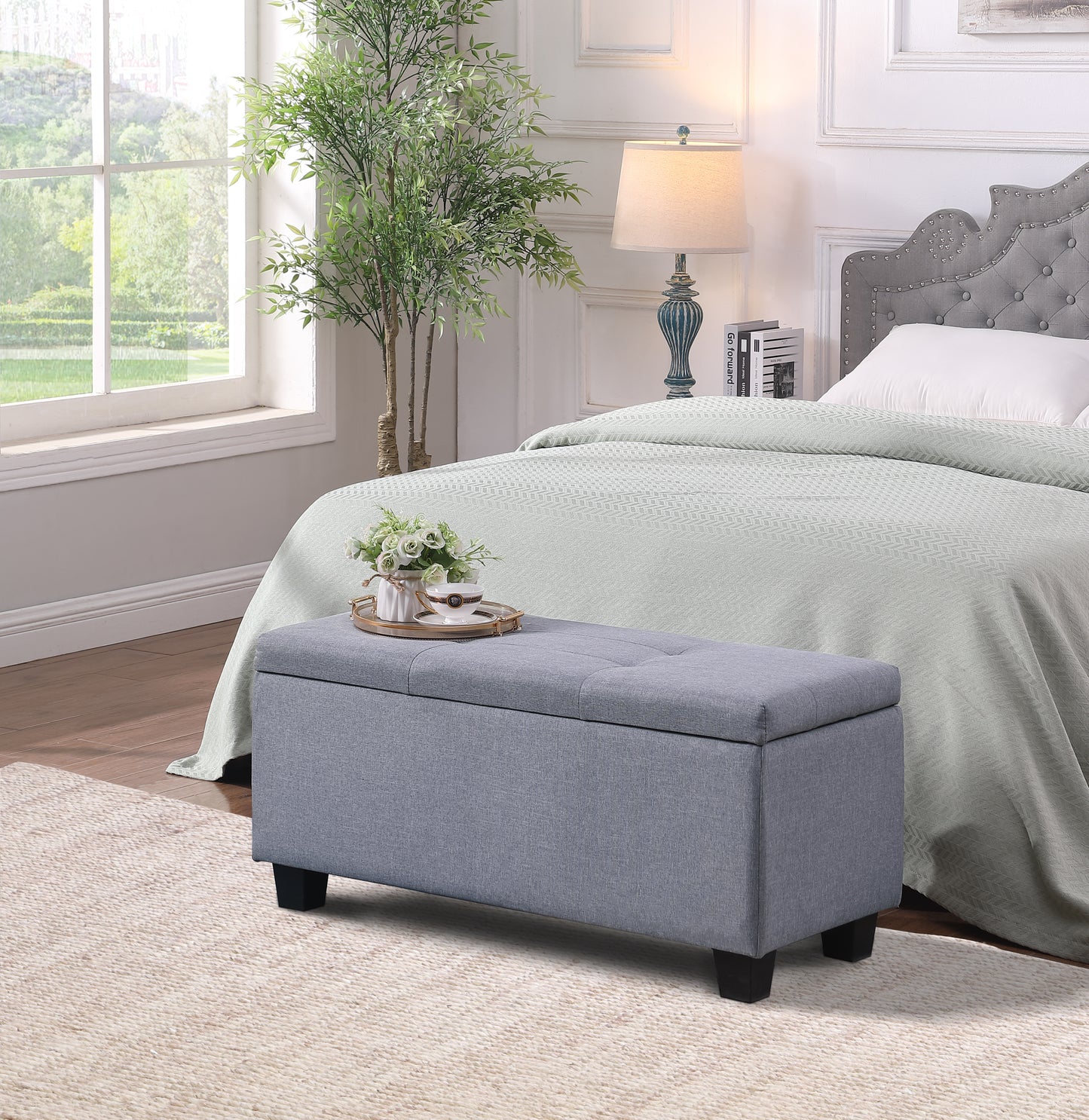 Grey tufted storage ottoman with dark wood legs and a tray with tea set
