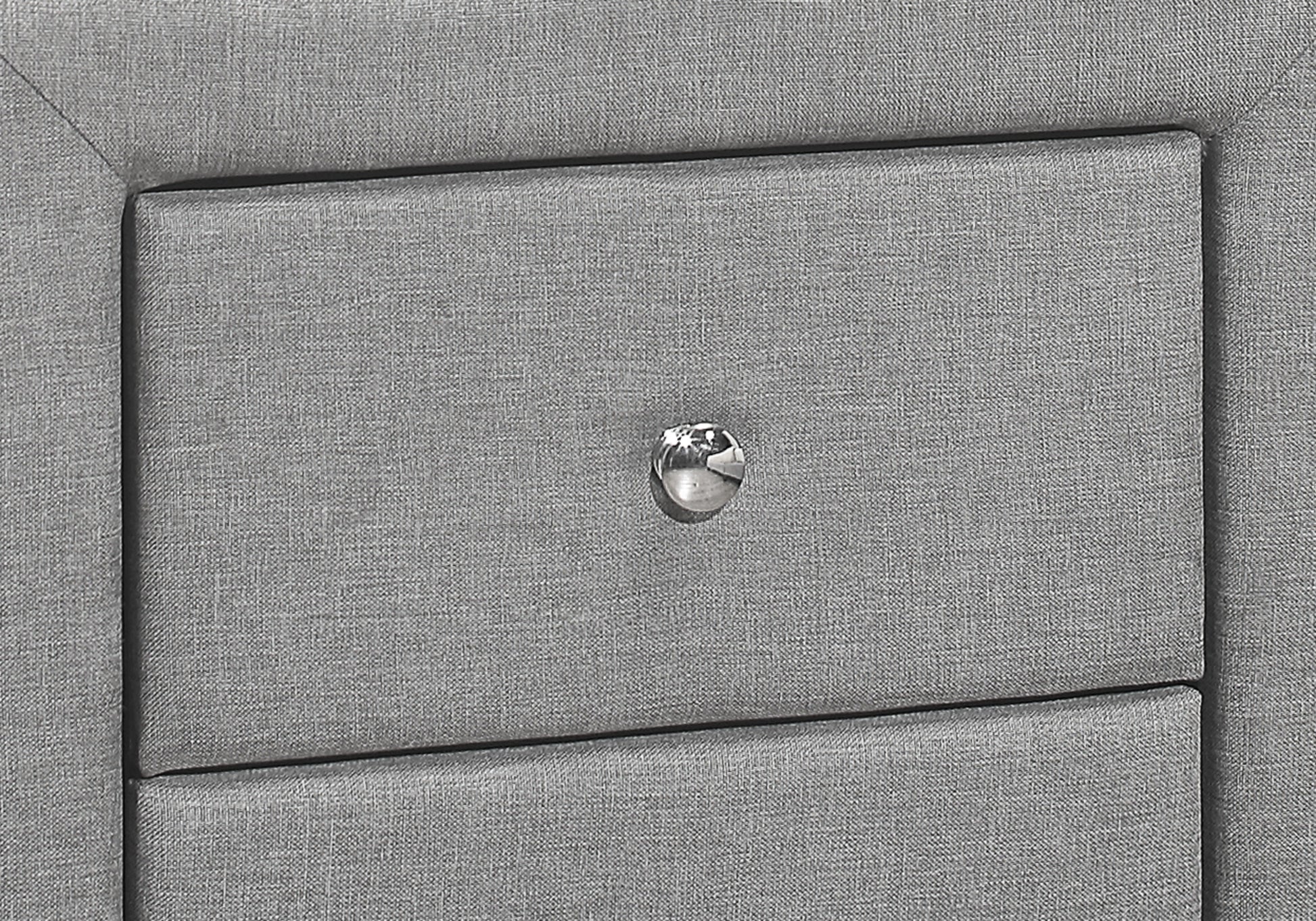Closeup of a textured grey upholstered nightstand with a crystal knob