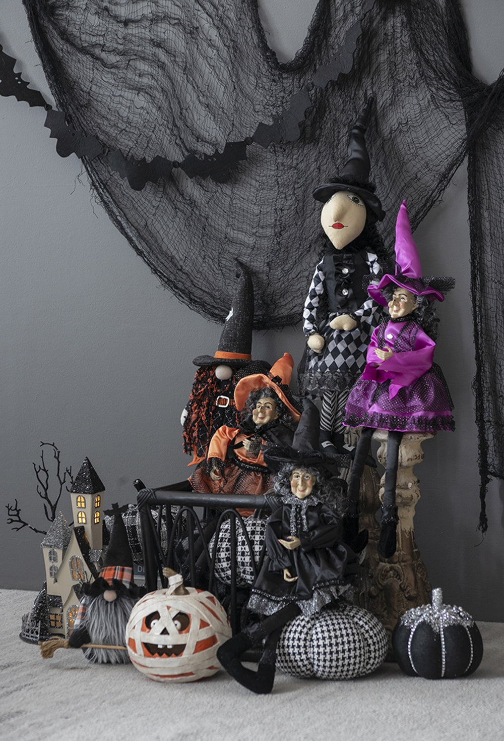 Five Halloween witch dolls in black and purple dresses with orange accents and spooky decorations