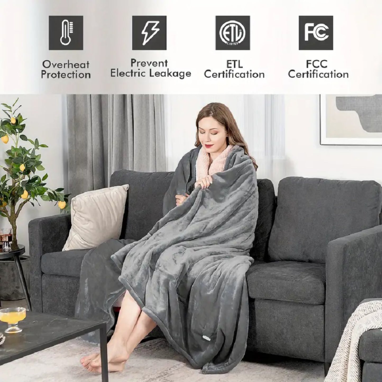 Cozy dark grey plush heated blanket draped over a woman on a sofa