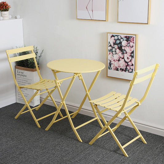 Yellow metal bistro set with a round table and two folding chairs on a grey rug